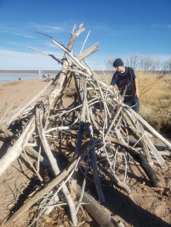 An AXL CAP student builds a shelter from driftwood.