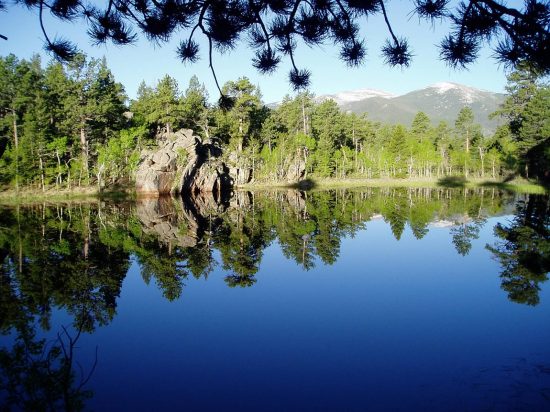 A scenic view of a pristine, still lake reflecting the trees and rocks that surround it