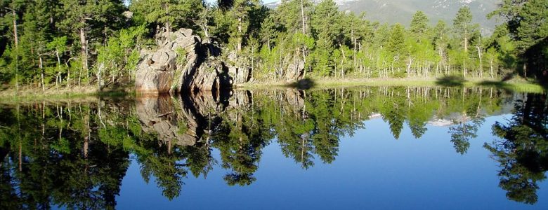 A scenic view of a pristine, still lake reflecting the trees and rocks that surround it